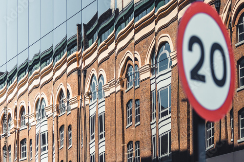 Close up shot of speed limit sign in an urban environment. Blurred background with mirrored facade reflecting a classical building. Driving limitations, social rules, European laws. 