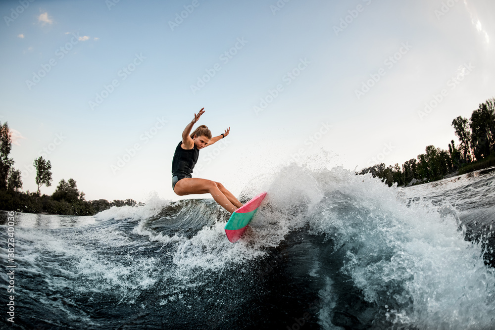 handsome woman balanced on surf style wakeboard on splashed river wave