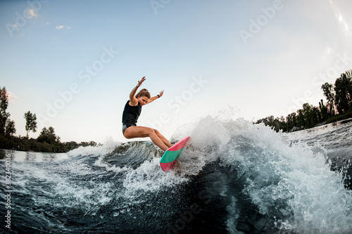 handsome woman balanced on surf style wakeboard on splashed river wave