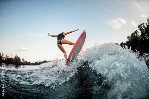 active girl on bright surf style wakeboard and jumps over splashing river water