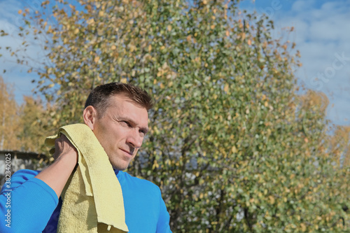 Handsome sportsman wipe sweat from a neck with towel, tilt head and looking tired after good, productive workout, outdoors exercise on a stadium in autumn season