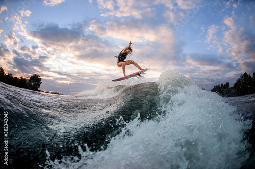 Photography view of woman jumping over big splashing wave on surf style wakeboard