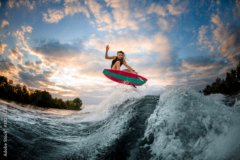 great view of woman jumping over big splashing wave on surf style wakeboard.