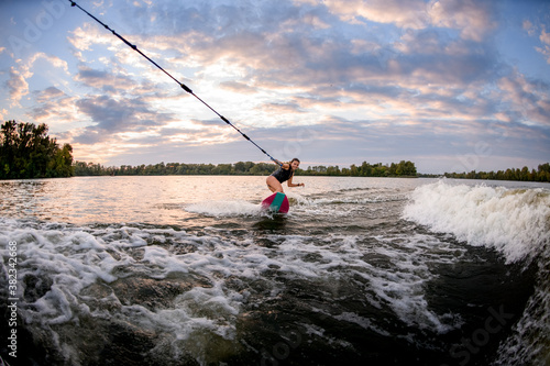 view of smiling woman riding on surf style wakeboard and holding tight rope