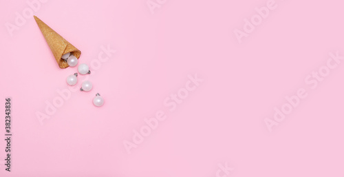 White glitter Christmas decoration baubles roll out of ice cream cone on pastel pink background. Creative new year concept with copy space. Horizontal banner with flat lay. Top view, place for text