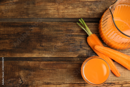 Jug and glass of freshly made carrot juice on wooden table, flat lay. Space for text