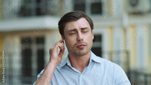 Portrait man walking with headphones at street. Man talking wireless earphones