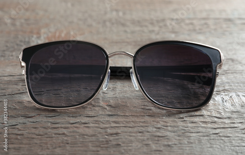 Stylish sunglasses on wooden background, closeup view