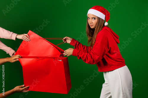 Beautifl girl with christmas hat drags red shopping bags on isolated green background photo