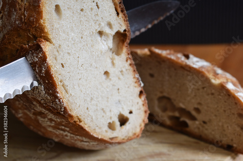 Bauernbrot angeschnitten in Makro, Schwarzes Brot wird mit Brotmesser geschnitten auf Holzbrett auf Holztisch vor schwarzem Hintergrund photo