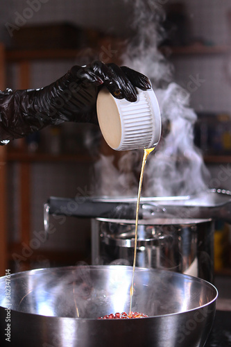 The chef adds olive oil to a metal bowl. Steam from the pan. Unrecognizable vertical photo.Hand in a black protective glove.