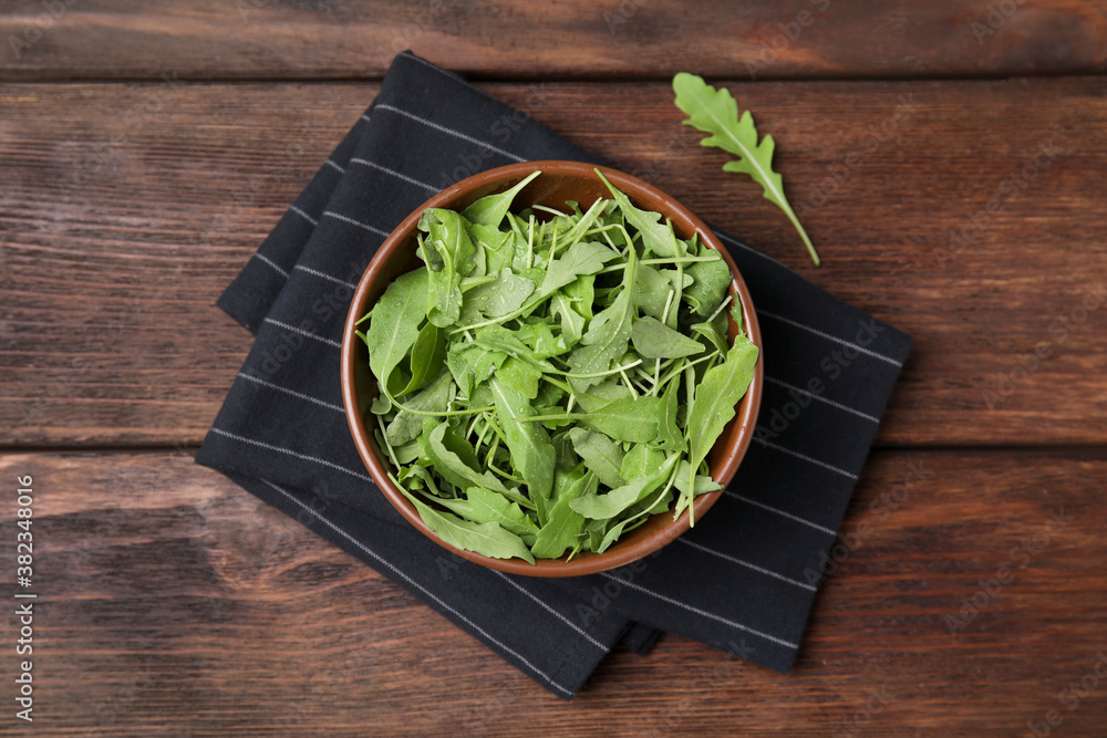 Fresh arugula leaves in bowl on wooden table, flat lay Fresh arugula leaves in bowl on wooden table, flat lay