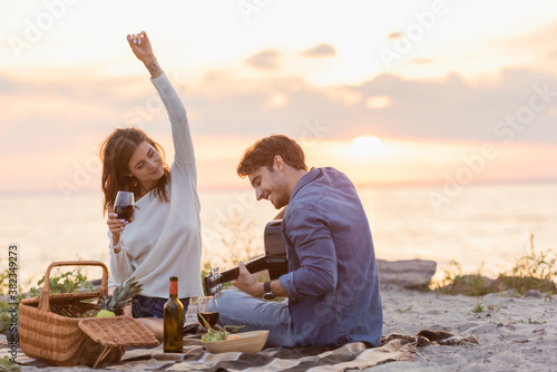 Selective focus of woman holding glass of wine near boyfriend playing acoustic guitar during picnic on beach © LIGHTFIELD STUDIOS