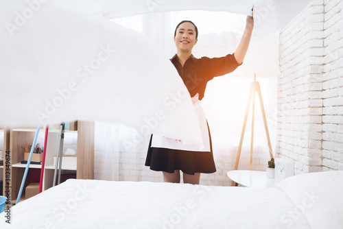 Bild auf Leinwand Cheerful housekeeper makes a bed in a large room.