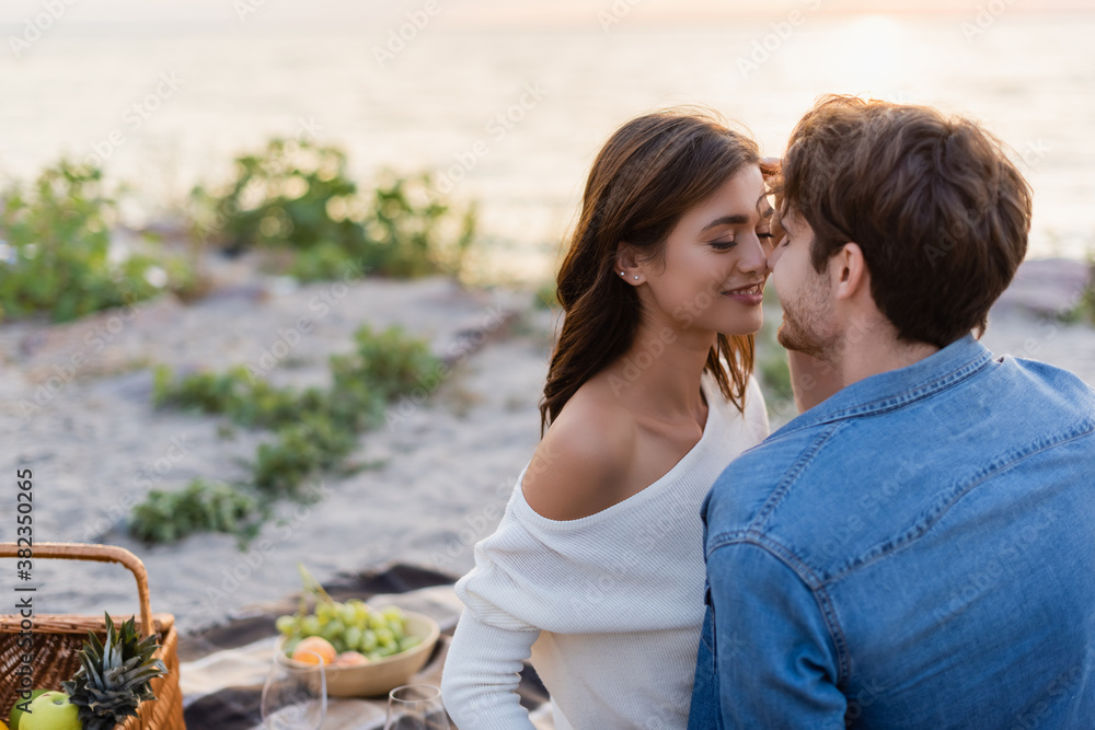 Man kissing girlfriend during picnic on beach at sunset