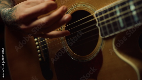 Unrecognizable person playing acoustic guitar in dark recording studio.
