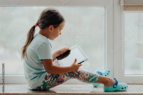 European Little Girl with Tablet pc Relaxing in a spacious room near the Window.   photo