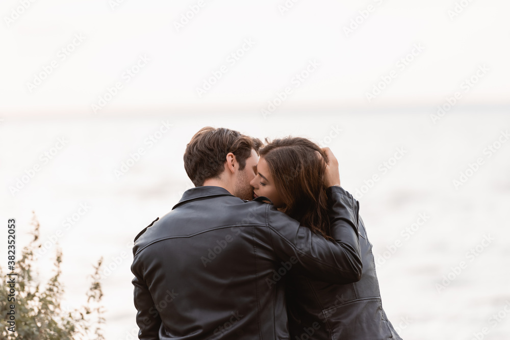 Back view of young couple in leather jackets kissing near sea