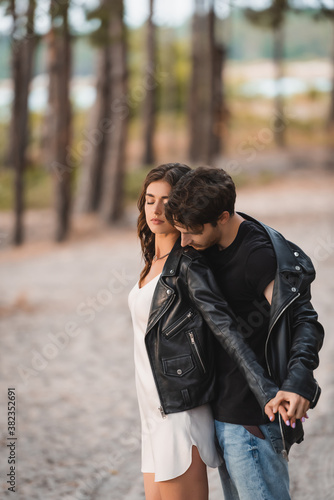 Man holding hand of brunette girlfriend in leather jacket in forest