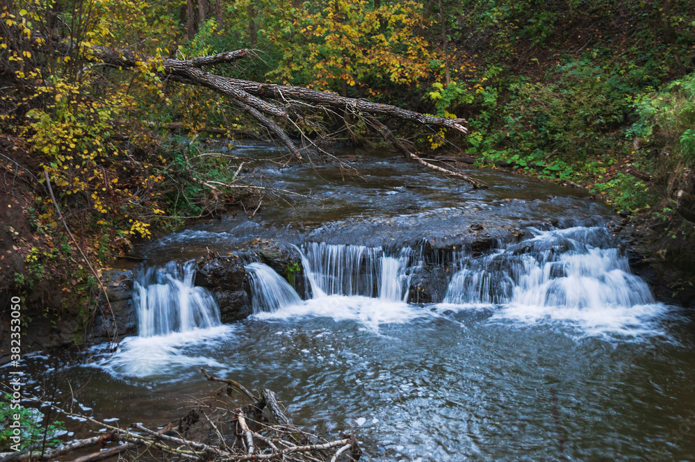 Autumn landscape with a river and a waterfall in the forest.