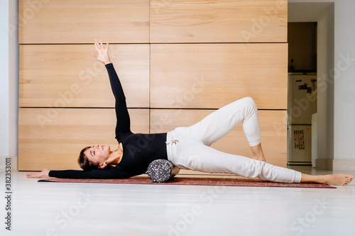 Woman using foam roller for myofascial release exercise for psoas square muscle on mat at home, after fitness exercise, muscle strain after high-intensity workout, overcome pain, rehabilitation concep photo