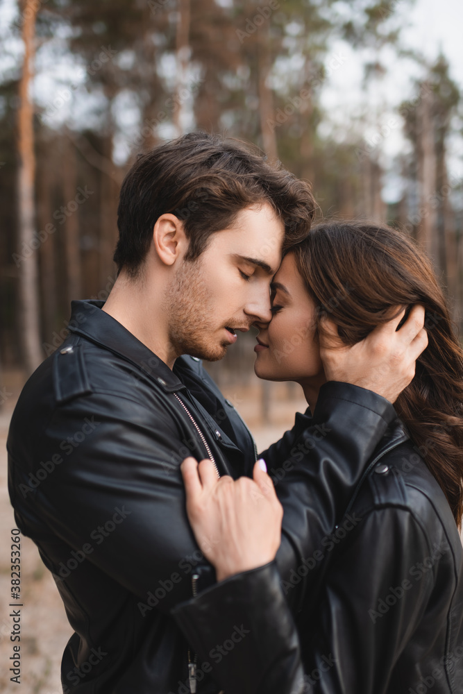 Side view of young man touching hair of girlfriend in leather jacket in forest