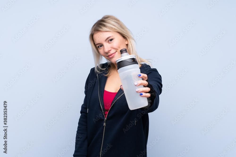 Obraz premium Young sport blonde woman over isolated blue background with sports water bottle