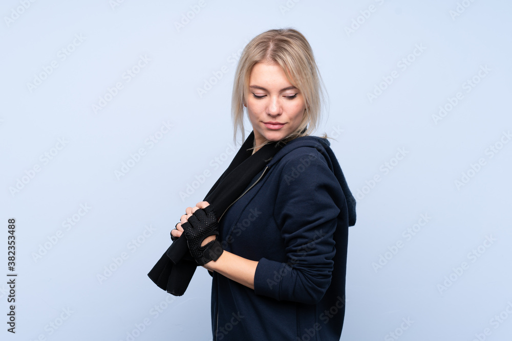 Young sport blonde woman over isolated blue background with sport towel Young sport blonde woman over isolated blue background with sport towel