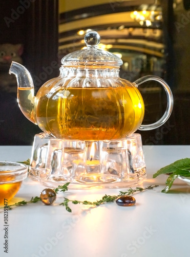 Fragrant fresh herbal tea and melissa in a glass teapot warming on a candle on a white table. Traditional herbal drink. Tea with honey. Kettle warmer