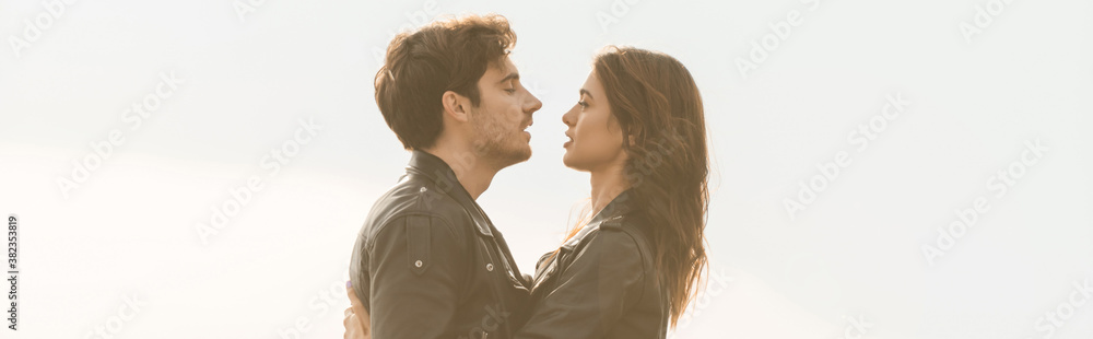 Panoramic crop of young couple in leather jackets looking at each other with sky at background Panoramic crop of young couple in leather jackets looking at each other with sky at background