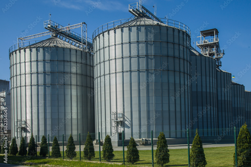 A large modern agro-processing plant for the storage and processing of grain crops. Fragment of large metal barrels of grain. Granary elevator. Horizontal image. A large modern agro-processing plant for the storage and processing of grain crops. Fragment of large metal barrels of grain. Granary elevator. Horizontal image.