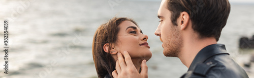 Website header of man in leather jacket touching cheek of girlfriend near sea