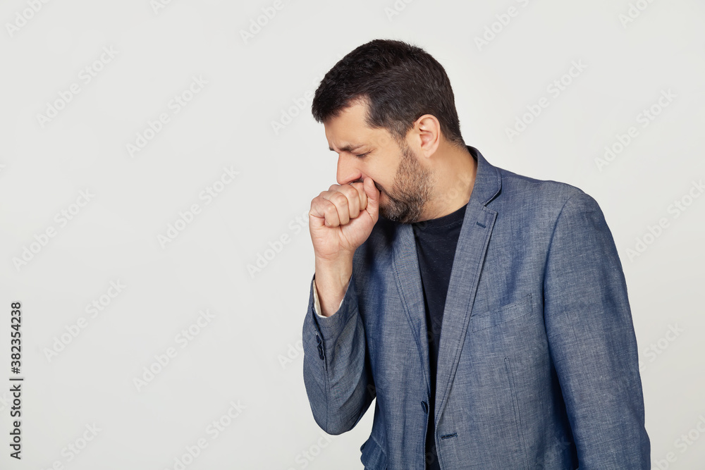 Young businessman man with a beard in a jacket, feeling unwell and coughing as a symptom of a cold or bronchitis. Health care concept. Portrait of a man on a gray background Young businessman man with a beard in a jacket, feeling unwell and coughing as a symptom of a cold or bronchitis. Health care concept. Portrait of a man on a gray background