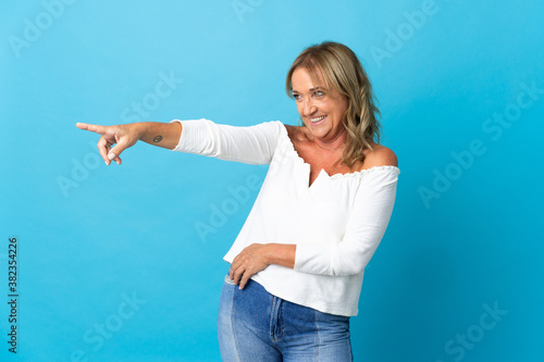 Middle aged blonde woman over isolated background pointing finger to the side and presenting a product