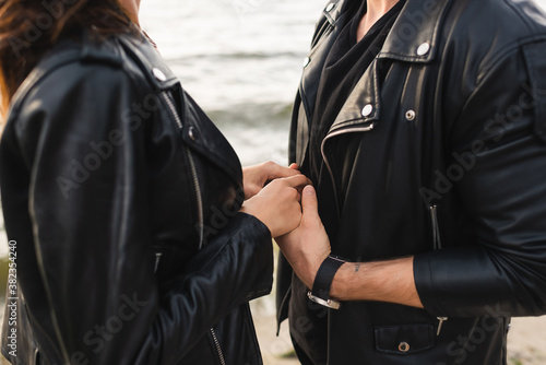 Cropped view of couple in leather jackets holding hands near sea