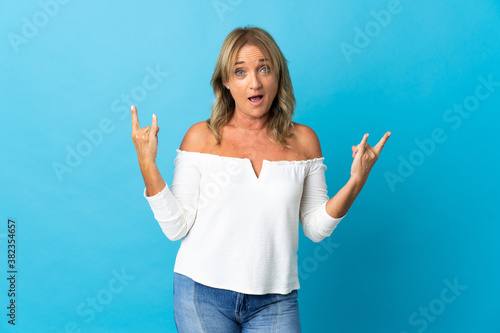 Middle aged blonde woman over isolated background making horn gesture
