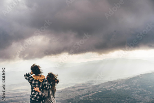 Couple on top of a mountain enjoying valley view before sunset.
