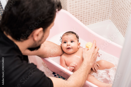 Father cleaning little baby at home bathtub