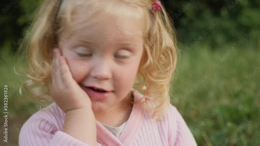 Lovely blonde girl 2 years old cute smiling looking to the side holding her face with her hand in the park Lovely blonde girl 2 years old cute smiling looking to the side holding her face with her hand in the park