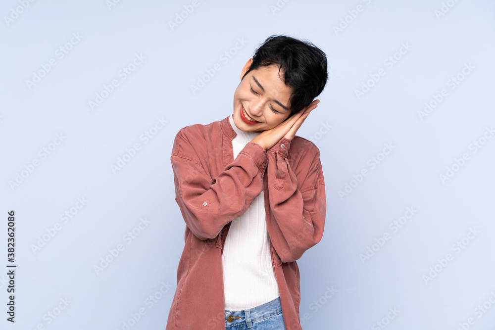 Young Asian girl over isolated blue background making sleep gesture in dorable expression Young Asian girl over isolated blue background making sleep gesture in dorable expression