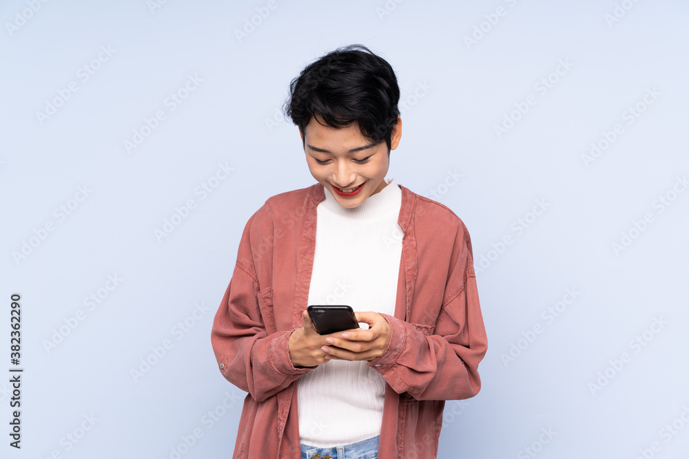 Young Asian girl over isolated blue background sending a message with the mobile Young Asian girl over isolated blue background sending a message with the mobile