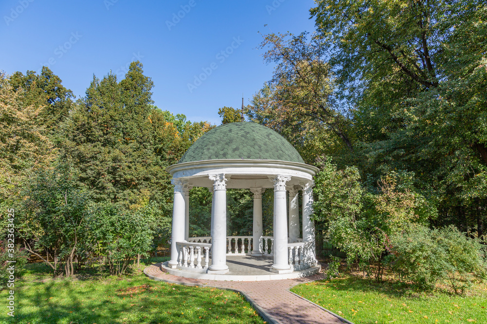 A gazebo made of white stone in a green park for rest and relaxation of visitors