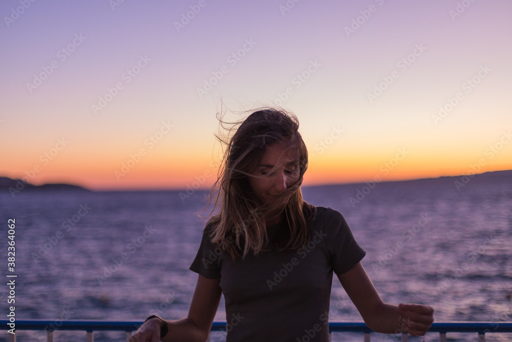 Young woman in front of the sea on a windy summer evening as the sun sets at blue hour