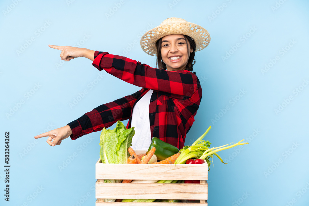 Young farmer Woman holding fresh vegetables in a wooden basket pointing finger to the side and presenting a product