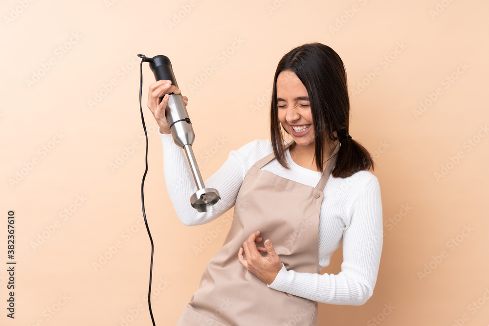 Young brunette girl using hand blender over isolated background making guitar gesture Young brunette girl using hand blender over isolated background making guitar gesture