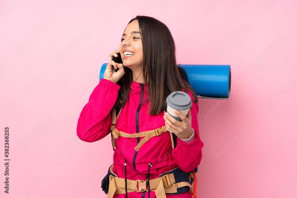 Young mountaineer girl with a big backpack over isolated pink background holding coffee to take away and a mobile Young mountaineer girl with a big backpack over isolated pink background holding coffee to take away and a mobile
