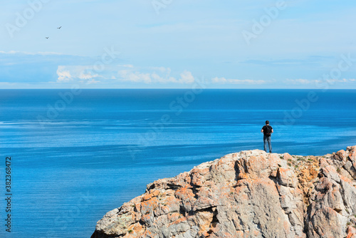 Man standing on a rock and admiring beautiful view on the Baikal Lake – the largest freshwater lake in the world. Travel concept. Majestic landscape of Siberian Lake. Image for card or poster.