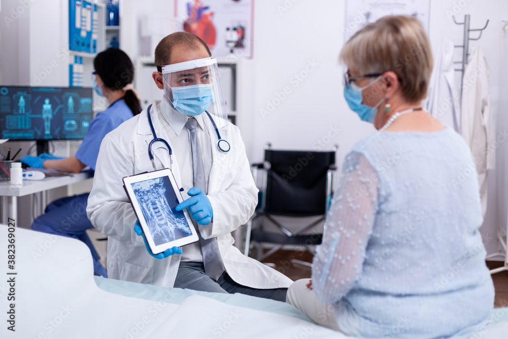 Discussing neck injury with female patient pointing tablet pc and wearing protective visor. Medical examination for infections, disease and diagnosis. Discussing neck injury with female patient pointing tablet pc and wearing protective visor. Medical examination for infections, disease and diagnosis.