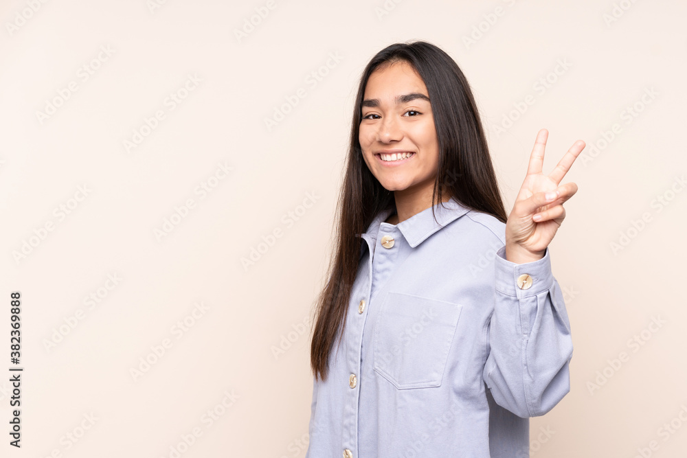 Young Indian woman isolated on beige background smiling and showing victory sign Young Indian woman isolated on beige background smiling and showing victory sign
