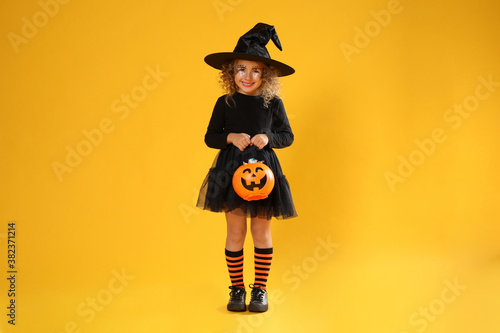 Slika na platnu Cute little girl with pumpkin candy bucket wearing Halloween costume on yellow b